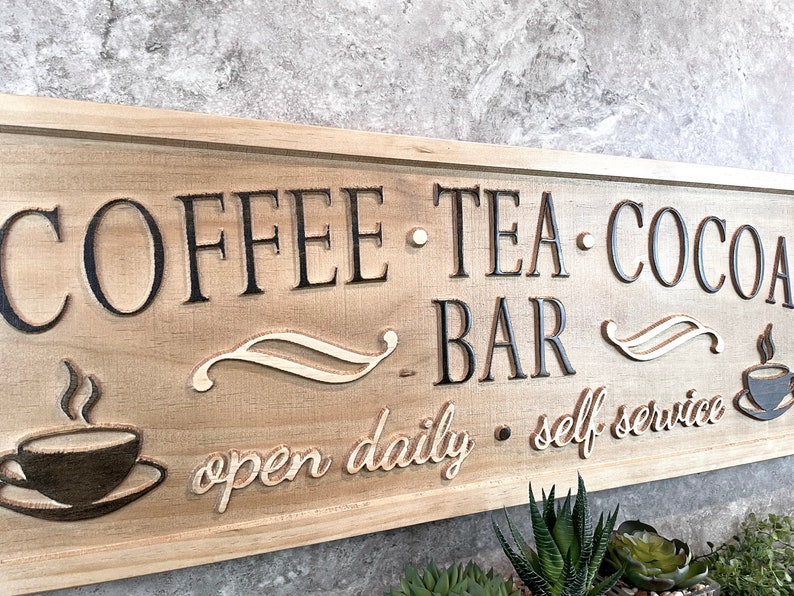 K&ouml;nnte beinhalten: Ein Holzschild mit dem Text "COFFEE - TEA - COCOA BAR" und "open daily - self service". Das Schild ist braun mit schwarzer Beschriftung und einem wei&szlig;en Design.