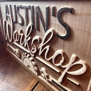 May include: A wooden sign with the text "Austin's Workshop" in black lettering. The sign is decorated with a saw blade and other tools.