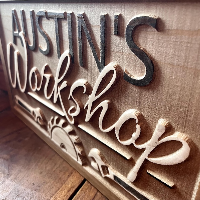 May include: A wooden sign with the text "Austin's Workshop" in black lettering. The sign is decorated with a saw blade and other tools.