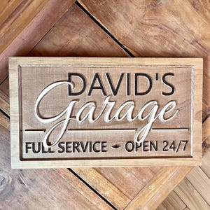 May include: A wooden sign with the text "DAVID'S Garage" in white lettering on a brown background. The sign also says "FULL SERVICE - OPEN 24/7".