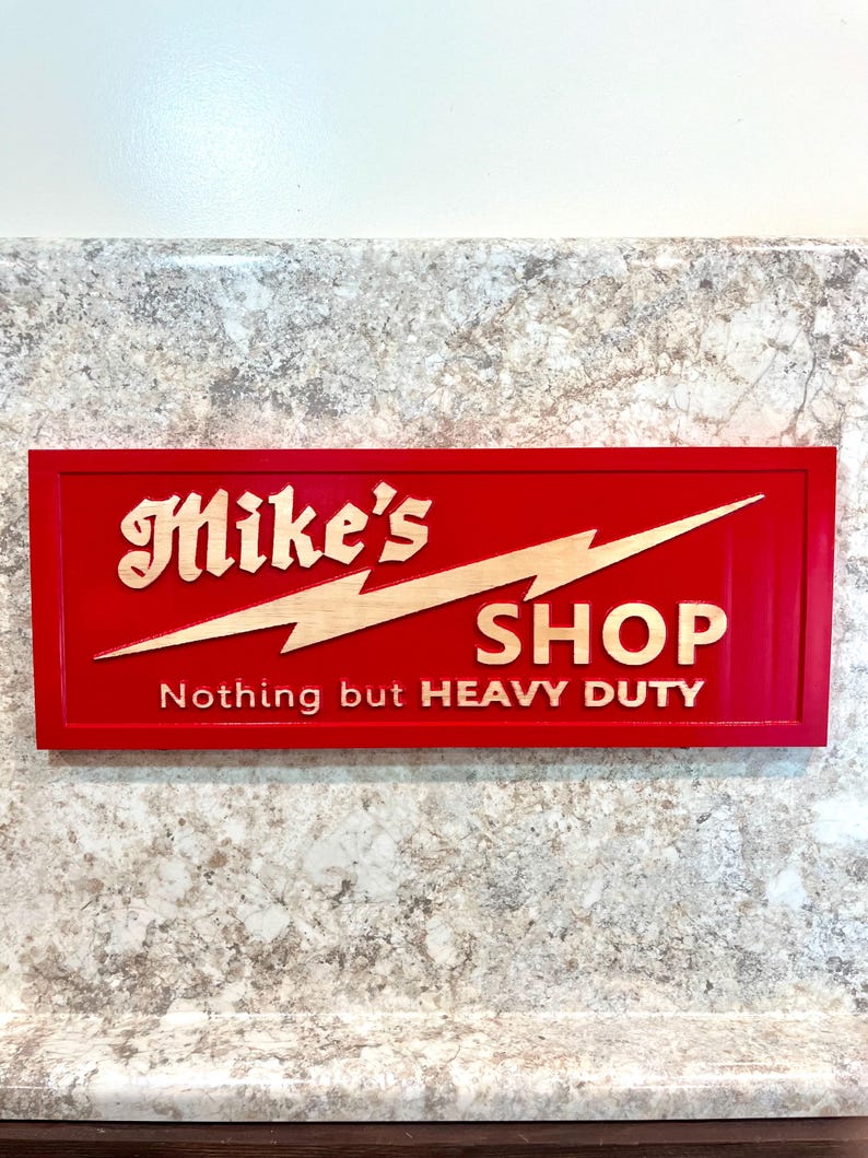 May include: Red wooden sign with the text "Mike's Shop" and the words "Nothing but HEAVY DUTY" in gold lettering. A lightning bolt graphic is above the word "Shop".