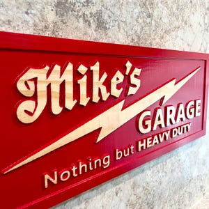 May include: Red wooden sign with white lettering that reads "Mike's Garage Nothing but Heavy Duty". A lightning bolt is depicted in the background.