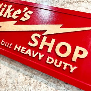 May include: Red wooden sign with a lightning bolt and the text "Mike's Shop Heavy Duty" in a light wood color.