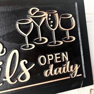 May include: Black wooden sign with the text "Open daily" and a graphic of five wine glasses. The sign has a rustic, distressed look.