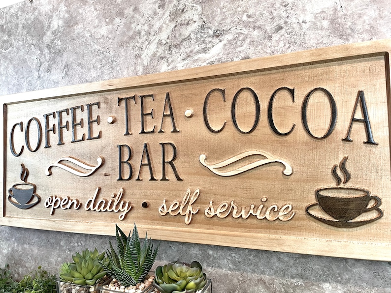 K&ouml;nnte beinhalten: Ein Holzschild mit dem Text "COFFEE TEA COCOA BAR open daily self service" in schwarzer Schrift. Das Schild hat eine braune Holzmaserung und zeigt zwei stilisierte Kaffeetassen mit aufsteigendem Dampf.