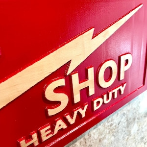 May include: Red wooden sign with a yellow lightning bolt and the words "SHOP HEAVY DUTY" in white lettering.