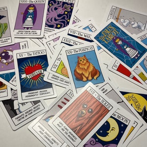 May include: A close-up of a deck of tarot cards with colorful illustrations and text. The cards are spread out on a white surface. The cards feature a variety of themes, including animals, nature, and abstract concepts. The text on the cards includes the names of the cards and their corresponding numbers.