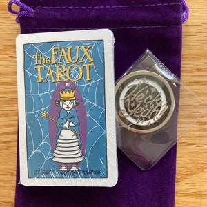 May include: A purple velvet bag with a drawstring closure contains a deck of cards with the title "The Faux Tarot" by Sammy Stein Bartholomew and a silver charm with the word "Heck Yeah!" in black lettering.