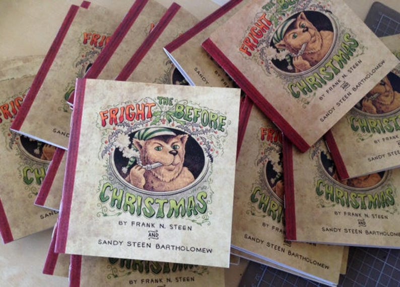 May include: A stack of paperback books with red spines. The cover of the top book features a cartoon illustration of a creature with a red hat and a green scarf. The title of the book is "The Fright Before Christmas" by Frank N. Steen and Sandy Steen Bartholomew.