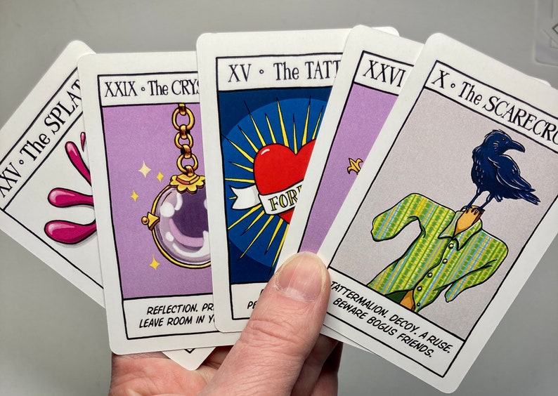 May include: Four tarot cards with purple backgrounds and colorful illustrations. The cards are titled "XV. The Splat", "XXIX. The Crystal", "XV. The Tattoo", and "X. The Scarecrow". The cards feature a pink splatter, a crystal ball on a chain, a heart with the word "Forever" on it, and a scarecrow with a crow on its head.