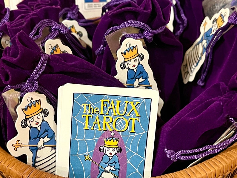 May include: Purple velvet bags with a white card that says "The Faux Tarot" and a cartoon illustration of a queen holding a scepter.