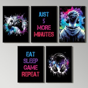 May include: Set of five framed art prints with a gaming theme. Each print features a black background with colorful splatter effects. Images include a game controller, headphones, and text that reads "JUST 5 MORE MINUTES" and "EAT SLEEP GAME REPEAT".