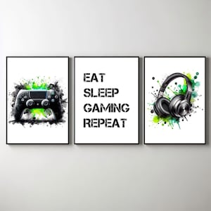 May include: Three black framed prints with white backgrounds and green and black watercolor splashes. The left print features a black video game controller. The middle print has the text "EAT SLEEP GAMING REPEAT". The right print features a pair of black headphones.