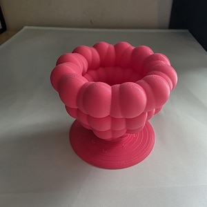 Puede incluir: Un cuenco decorativo rosa vibrante con un diseño único en forma de nube. El cuenco presenta una base redondeada y un borde texturizado y burbujeante. Esta llamativa pieza es perfecta para exhibir objetos pequeños o como objeto de arte independiente.