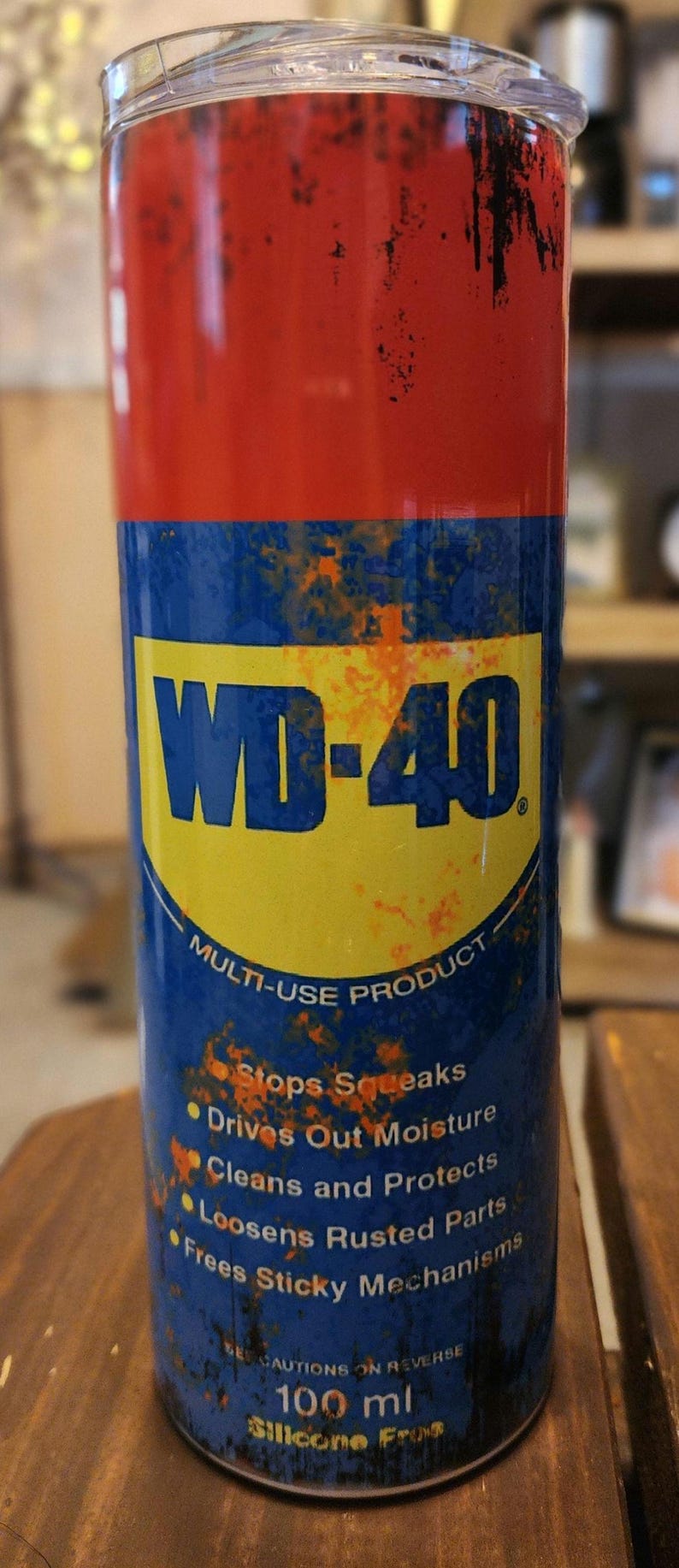 May include: A cylindrical tumbler with a red top and blue base, featuring the WD-40 logo and product information. The design includes text about the product's multi-use capabilities. The tumbler is approximately 100 ml.