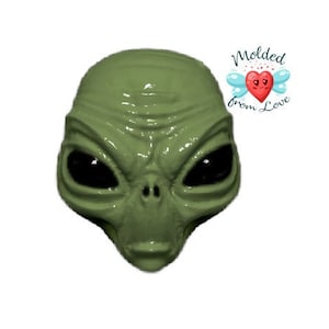 May include: Green alien face with large black eyes and a textured surface. The alien face is a 3D printed object.
