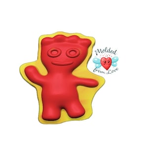Peut inclure: Moule en forme de bonbon gélifié rouge en forme de personnage de dessin animé avec un grand sourire et deux yeux. Le moule est sur un fond jaune et le texte "Molded from Love" est dans le coin supérieur droit.
