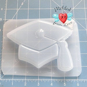 May include: A clear plastic mold shaped like a graduation cap. The mold is on a gray grid background. The text "Molded from Love" is visible in the upper right corner of the image.