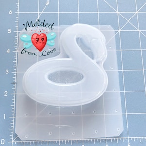 May include: A white silicone mold shaped like a flamingo pool float. The mold is on a gridded surface. The text "Molded from Love" is visible in the top left corner of the image.