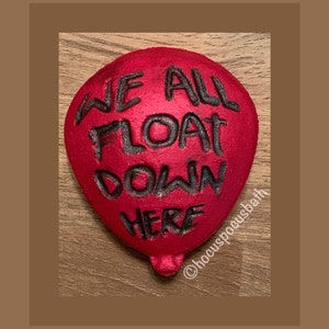 May include: Red bath bomb shaped like a balloon with the text "We All Float Down Here" in black lettering.