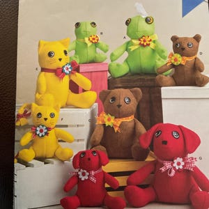 May include: A sewing pattern featuring various stuffed animal designs, including a green frog, brown bear, yellow cat, and red dog. Each plushie has a decorative bow. The pattern is labeled "Simplicity" and includes sizing information.