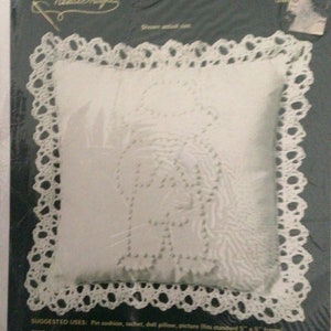 May include: A white pillow with a crocheted border and a candlewicking design of a tree. The kit includes fabric, yarn, lace, a needle, and instructions. The pillow is 5 inches by 5 inches.