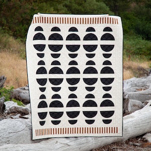 May include: A white quilt with a geometric pattern of black half circles. The quilt has a brown and white striped border.