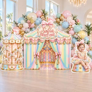 Può includere: Un set di decorazioni per feste a tema carnevalesco con una sagoma di giostra, uno sfondo centrale a forma di tendone con la scritta Sofia SWEET ONE e la sagoma di un bambino con un vestito a balze su una base, circondato da un arco di palloncini.