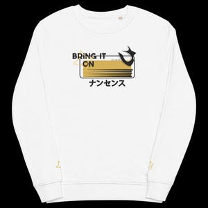 Könnte beinhalten: Weißer Langarm-Pullover mit einem gold-schwarzen Grafikdesign. Die Grafik zeigt den Text "BRING IT ON" und japanischen Text. Der Pullover hat goldene Stern-Details an den Ärmeln.