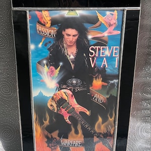 Puede incluir: Una imagen enmarcada de Steve Vai, un músico, sosteniendo una guitarra. La imagen está sobre un fondo de llamas y nubes. El texto "Steve Vai and Warfare" es visible en la imagen.