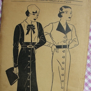 May include: A vintage sewing pattern featuring two women's dress designs. The dress on the left is a black dress with a white collar and a button-down front. The dress on the right is a white dress with a black collar and a button-down front. Both dresses have a skirt that falls to the knee. The pattern includes instructions in French and English.