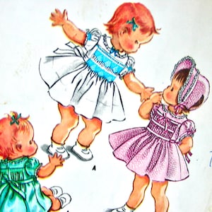 May include: Vintage sewing pattern for two little girls' dresses. The pattern includes a white dress with blue trim, a pink dress with white trim, and a hat. The pattern is printed with a transfer.