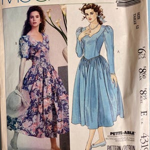 May include: A vintage McCall's sewing pattern with two dress designs. One dress is a blue floral print, the other is a solid light blue. The pattern includes the text "LAURA ASHLEY" and "4319".