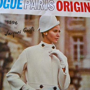 May include: Vintage Vogue Paris Original sewing pattern. The image features a woman wearing a cream-colored coat and hat. The coat has large dark buttons and a high collar. The text on the pattern reads "Vogue Paris Original" and "1596 by Jacques Griffe."
