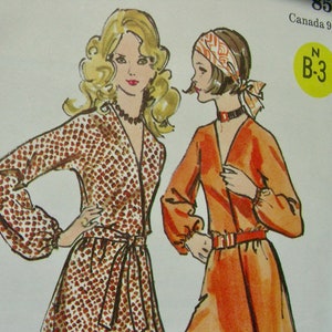 May include: Two vintage sewing patterns for dresses. The pattern on the left is brown with white polka dots. The pattern on the right is orange. Both patterns have long sleeves and a V-neckline. The pattern on the left has a tie belt. The pattern on the right has a belt. The pattern number is B-3.