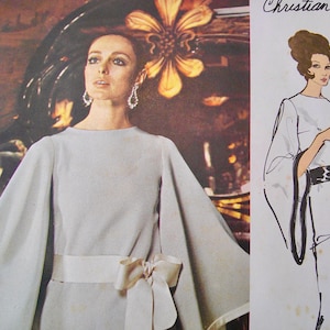 May include: A vintage fashion image featuring a woman in a light gray dress with wide sleeves and a matching bow belt. The image is next to a Christian Dior fashion illustration. The dress has a boat neck and a flowing silhouette.