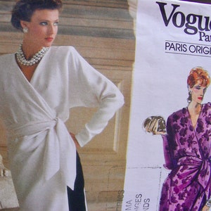 May include: Vogue Patterns Paris Original sewing pattern featuring two women wearing wrap dresses. The woman on the left is wearing a white wrap dress with a pearl necklace. The woman on the right is wearing a purple floral print wrap dress. The pattern is for a dress.