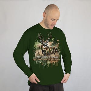 May include: A green long-sleeved shirt featuring a camouflage deer graphic and the text "CAMO KEEPS ME HIDDEN THE HUNT KEEPS ME ALIVE".