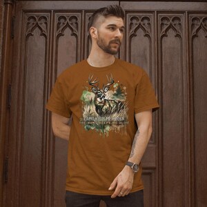 May include: A brown t-shirt featuring a camouflage print of a deer and the text "CAMO KEEPS ME HIDDEN THE HUNT KEEPS ME ALIVE".
