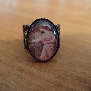 K&ouml;nnte beinhalten: Ein Bronzering mit einem Kamee, das eine Frau in einem rosa Kleid zeigt. Das Kamee ist in einem runden, ovalen Rahmen gefasst.