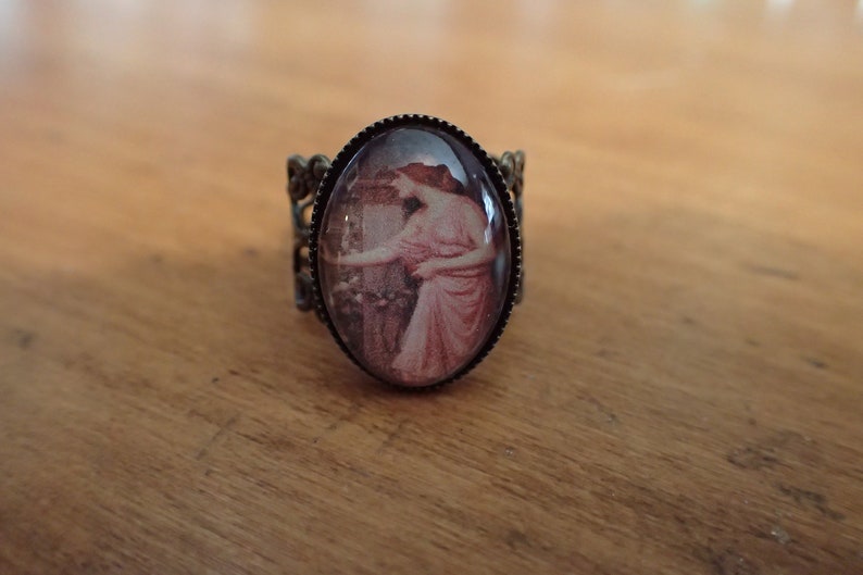 K&ouml;nnte beinhalten: Ein Bronzering mit einem Kamee, das eine Frau in einem rosa Kleid zeigt. Das Kamee ist in einem runden, ovalen Rahmen gefasst.
