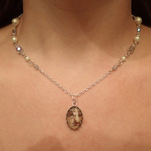 May include: A silver chain necklace with white pearl accents and a pendant featuring a vintage-style image of a woman in a dress.