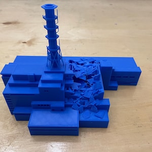 以下が含まれることがあります： 損傷した原子炉と高い煙突を持つ原子力発電所の青い3Dプリントモデルです。