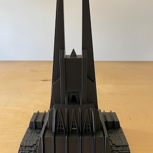May include: A black 3D printed model of a tall, pointed building with a geometric design. The building has a series of windows and a pointed roof.