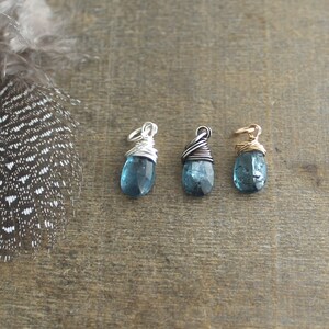 May include: Three teardrop-shaped blue topaz stones wrapped in wire, each with a different coloured wire: silver, gunmetal, and gold.