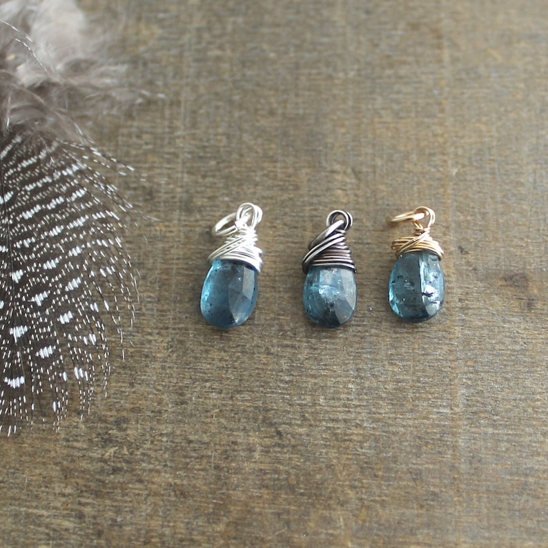 May include: Three teardrop-shaped blue topaz stones wrapped in wire, each with a different coloured wire: silver, gunmetal, and gold.
