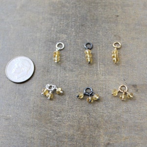 May include: Six different charms featuring small, round, golden citrine beads. Three charms have three beads, and three charms have a single bead.