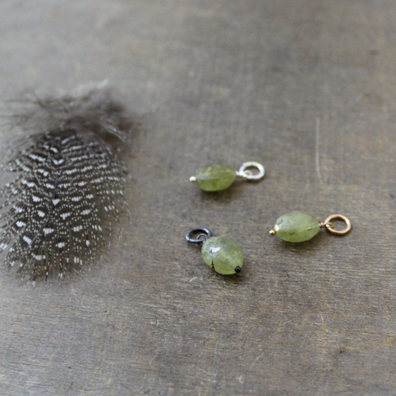 May include: Three green gemstone pendants with silver and gold accents. The pendants are on a wooden surface.