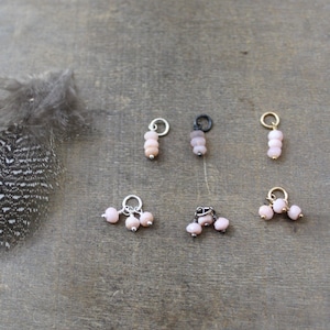 May include: A collection of six pink opal charm pendants with different styles of metal findings. The charms are arranged on a wooden surface.