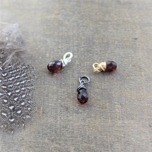 May include: Three small teardrop-shaped red gemstone pendants wrapped in silver, gold, and black wire.